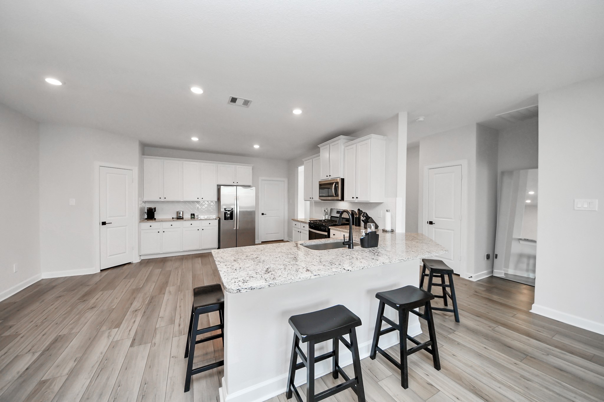 3006 Floating Barque Drive Santa Fe, TX 77510 - Photo 5 of 37 This modern kitchen features a spacious open layout with sleek white cabinetry, stainless steel appliances, and a large granite island with seating. Light wood flooring throughout and recessed lighting.