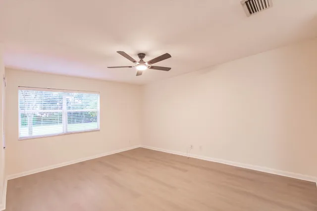 an empty room with chandelier fan and windows