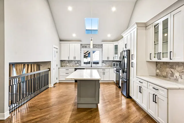 a open kitchen with kitchen island granite countertop a refrigerator oven a sink dishwasher and white cabinets with wooden floor