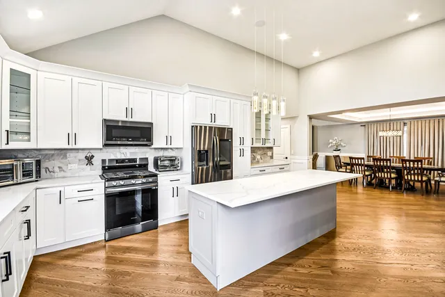 a large white kitchen with wooden floor and stainless steel appliances