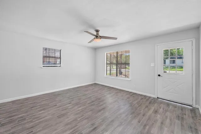 an empty room with wooden floor ceiling fan and windows