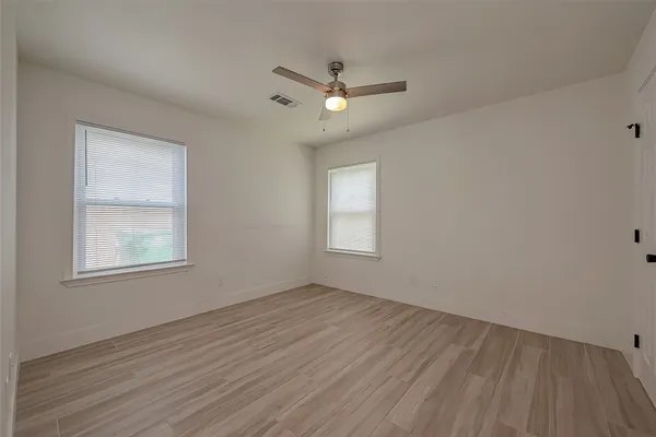 an empty room with wooden floor ceiling fan and windows