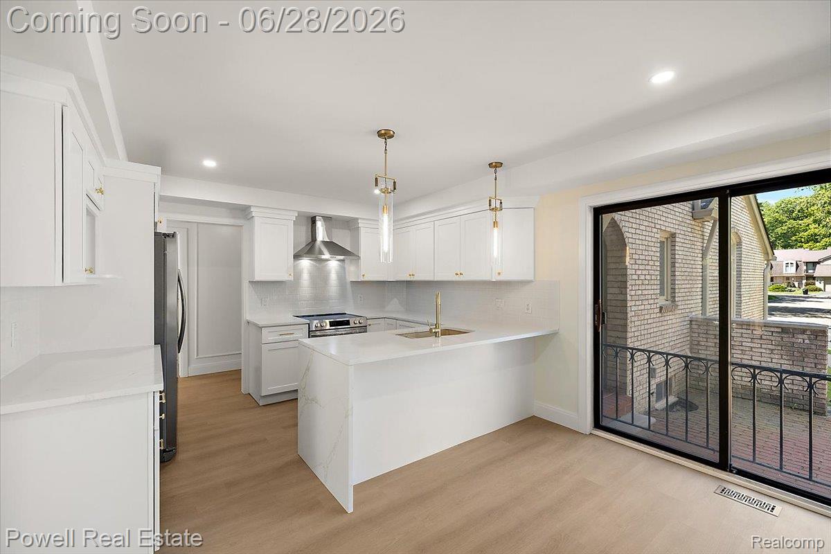 1447 Ravineview Court, Unit C12 Bloomfield Hills, MI 48304 - Photo 23 of 49 Bright kitchen featuring white cabinetry, a waterfall-edge island with seating, stainless steel appliances, and a sliding glass door opening to an outdoor patio with wrought iron railing