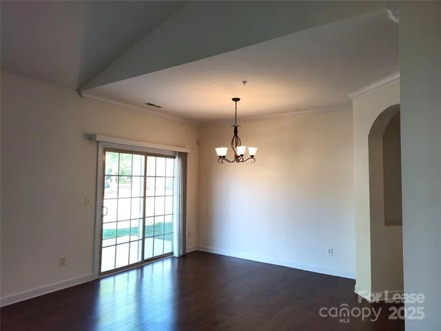 an empty room with wooden floor chandelier and windows