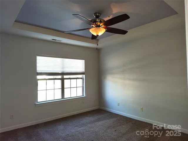 an empty room with a chandelier fan and windows
