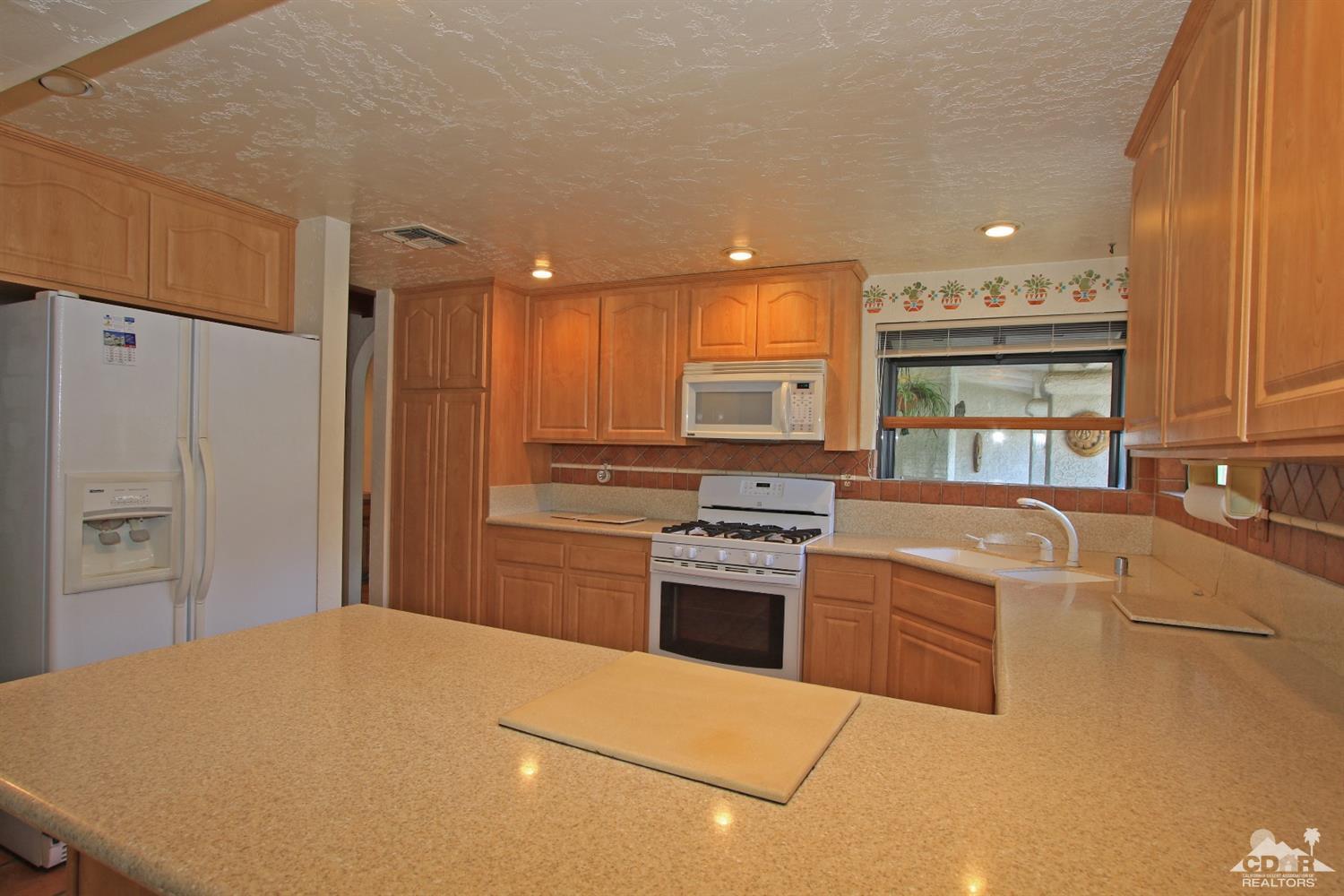 70400 Chappel Road Rancho Mirage, CA 92270 - Photo 23 of 49 a kitchen with stainless steel appliances granite countertop a stove a refrigerator a sink a oven with white cabinets and wooden floor