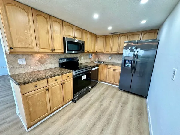 a kitchen with stainless steel appliances granite countertop a refrigerator a sink dishwasher a stove top oven a large island with wooden floor and cabinets