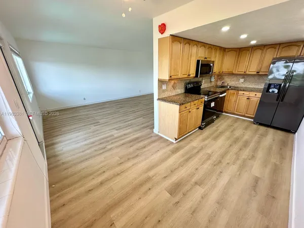 a kitchen with stainless steel appliances granite countertop a stove a sink a refrigerator white cabinets and wooden floor