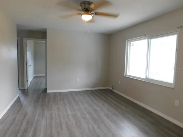 an empty room with wooden floor fan and windows