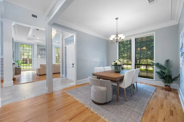 a dining room with wooden floor a chandelier a glass table and windows