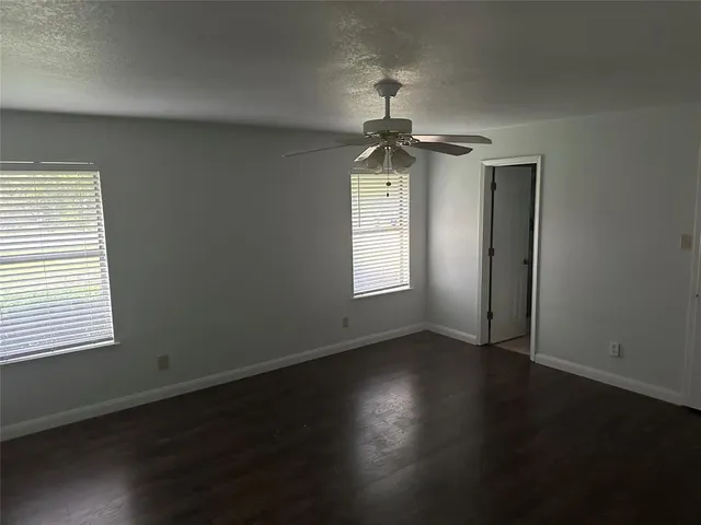 a view of a livingroom with wooden floor a ceiling fan and windows