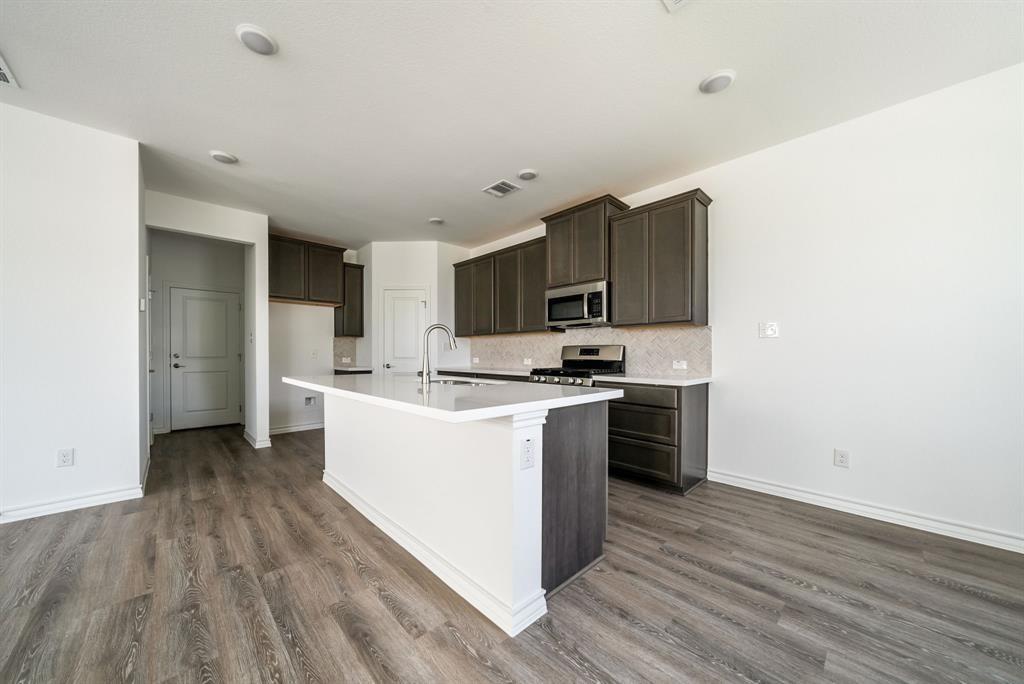 123 Watkinville Road Hutto, TX 78634 - Photo 6 of 30 Kitchen with dark wood finish cabinetry, stainless steel appliances, backsplash, and an island with sink