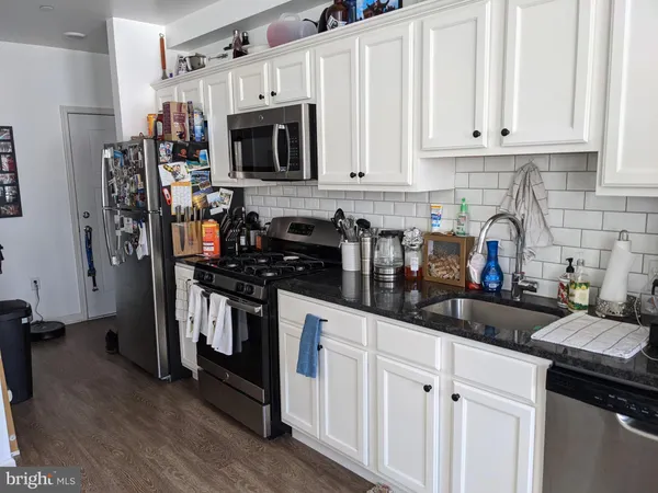 a kitchen with stainless steel appliances granite countertop a refrigerator a stove a sink and white cabinets