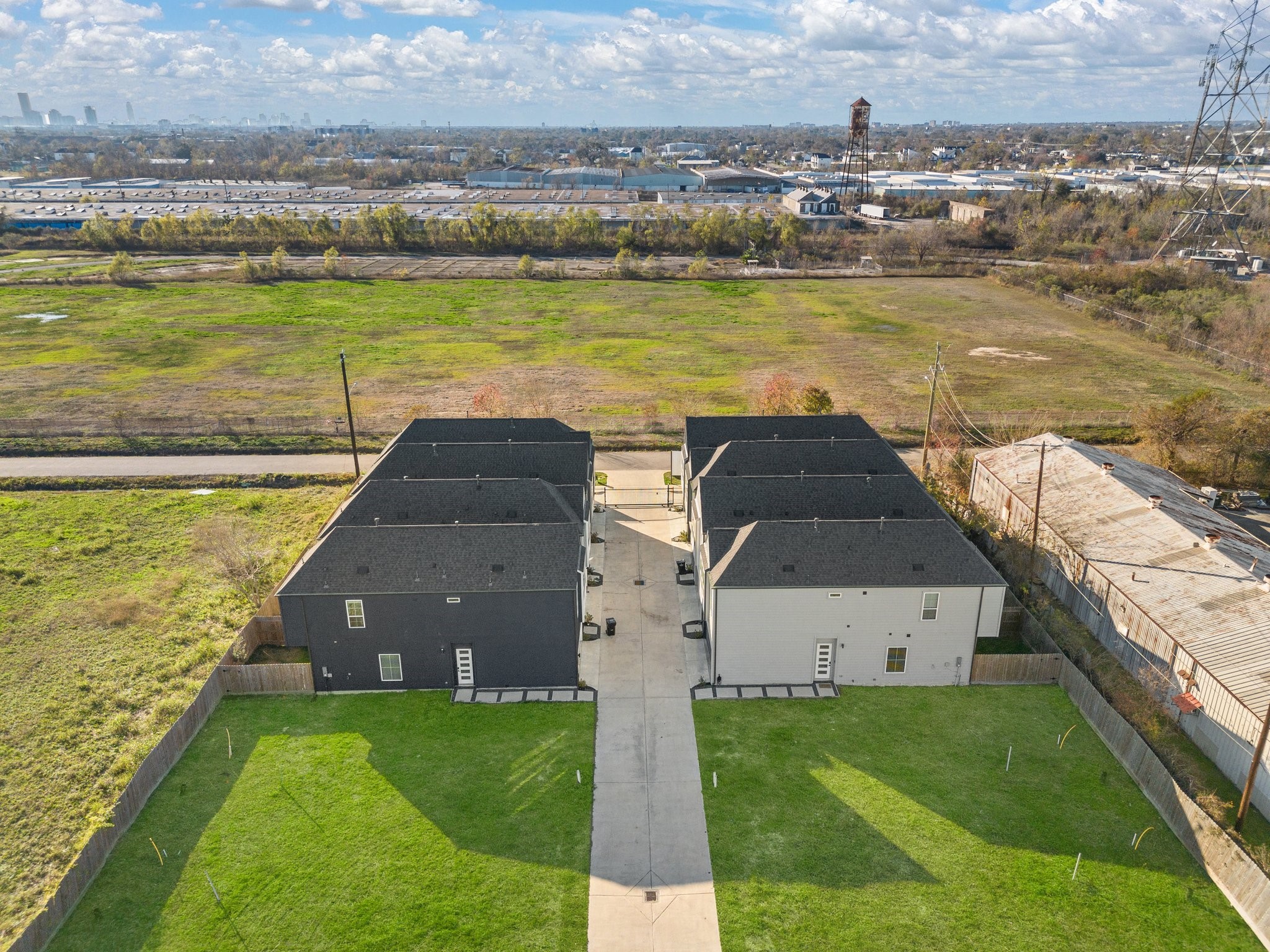 2928 Stevens Street Houston, TX 77026 - Photo 29 of 30 This aerial photo showcases a set of modern duplexes with a shared driveway, surrounded by green lawns and fenced backyards. It offers a spacious, open view of adjacent fields, with an industrial area in the distance.