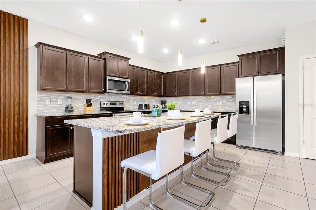 4494 Kaipo Road Davenport, FL 33897 - Photo 12 of 100 a kitchen with stainless steel appliances granite countertop a stove top oven a refrigerator a sink and a oven with wooden cabinets