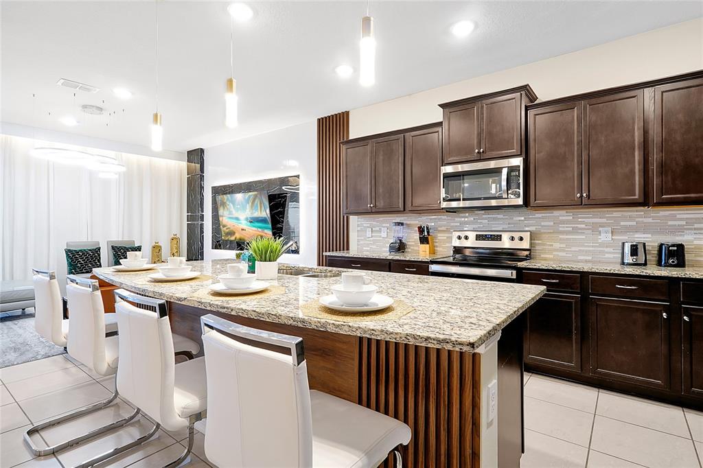4494 Kaipo Road Davenport, FL 33897 - Photo 15 of 100 a kitchen with stainless steel appliances granite countertop a stove a sink a microwave a refrigerator and cabinets