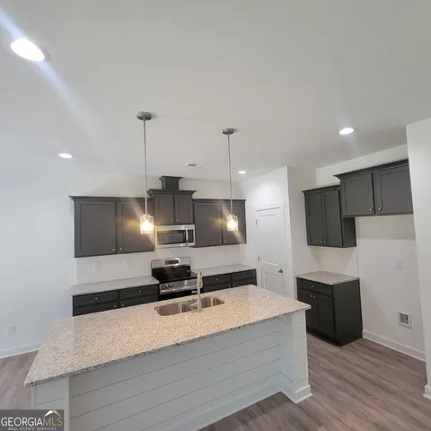 a large kitchen with a large counter top a sink stainless steel appliances and cabinets