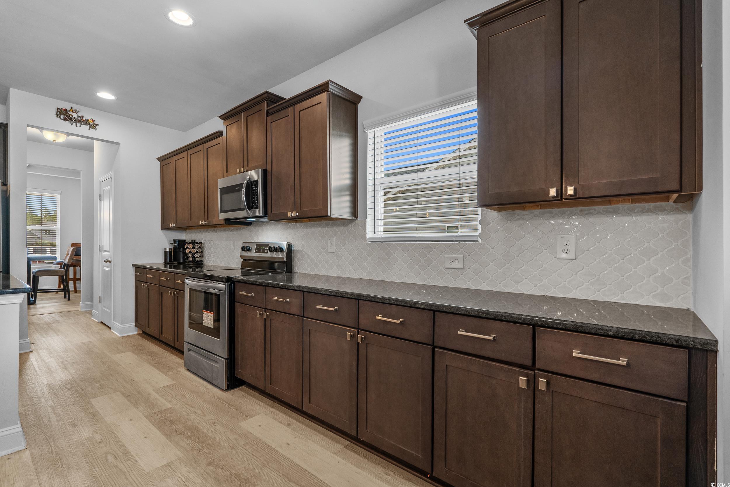 2064 Hazlette Loop Conway, SC 29526 - Photo 10 of 39 Kitchen featuring stainless steel appliances, dark brown cabinets, dark stone counters, light wood-style floors, and backsplash