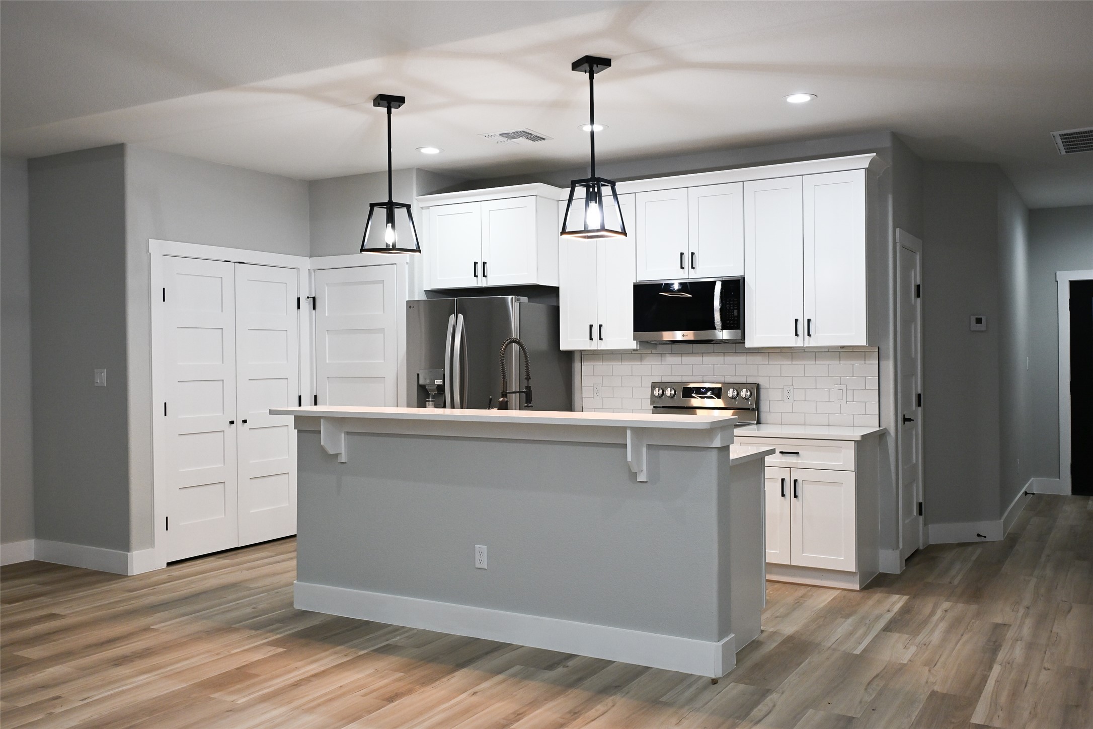 516 North Hackberry Avenue Luling, TX 78648 - Photo 28 of 36 Kitchen featuring appliances with stainless steel finishes, white cabinetry, decorative backsplash, a kitchen island with sink, and hanging light fixtures