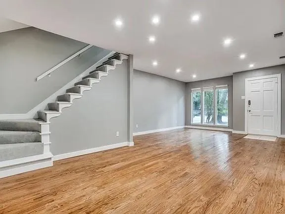 a view of an empty room with wooden floor and stairs