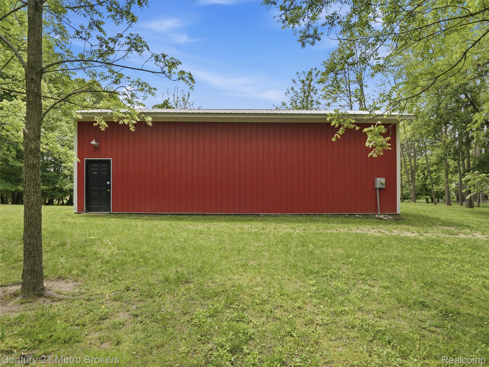 11447 North Latson Road Linden, MI 48451 - Photo 43 of 52 Red metal siding structure with a white corrugated roof, featuring a black entry door and exterior lighting