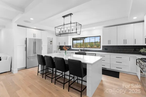 a kitchen with stainless steel appliances granite countertop a stove top oven a refrigerator a sink and a dining table with white cabinets