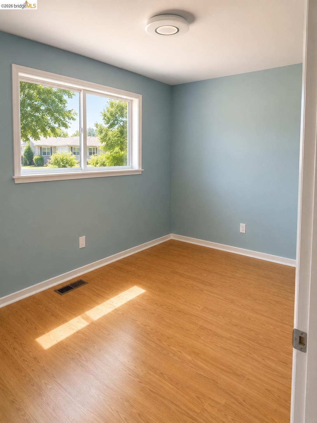 269 Crescent Drive Rio Vista, CA 94571 - Photo 7 of 9 Room with light blue walls, wood-finish flooring, a white trim window, and a modern flush-mount ceiling light fixture