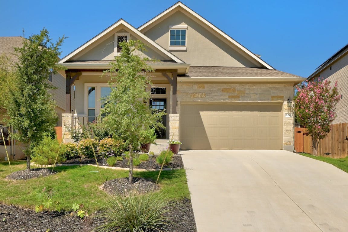 View of front facade featuring stone siding, an attached garage, driveway, and stucco siding