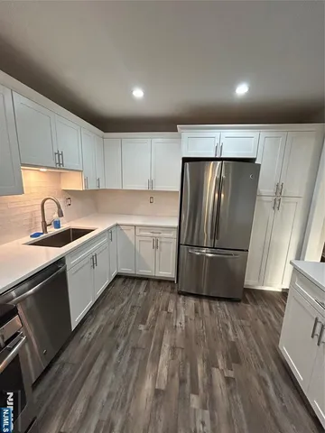 a kitchen with stainless steel appliances granite countertop a sink a stove a refrigerator with grey cabinets and wooden floor