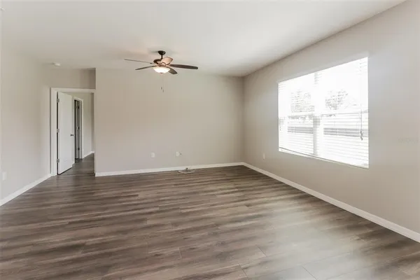 an empty room with wooden floor ceiling fan and windows