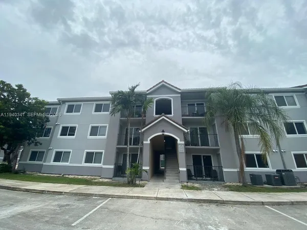 a front view of a building with lot of cars and trees