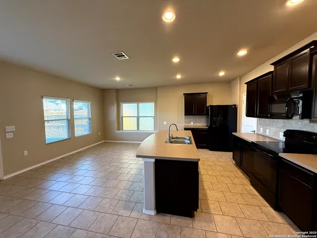 a large kitchen with kitchen island granite countertop a stove a sink a counter top space and cabinets