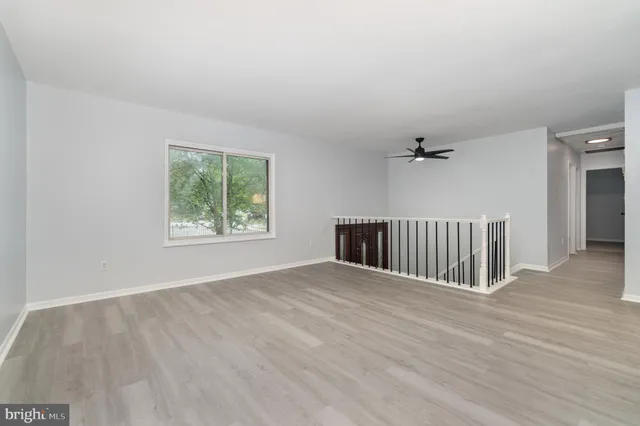 an empty room with wooden floor fan and windows