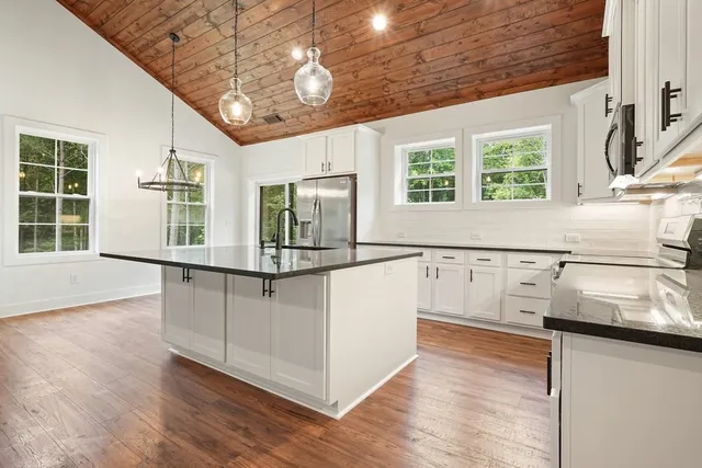 a kitchen with stainless steel appliances granite countertop a stove a sink and white cabinets with wooden floor