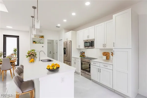 a kitchen with stainless steel appliances kitchen island granite countertop a refrigerator a stove a sink dishwasher and white cabinets with wooden floor