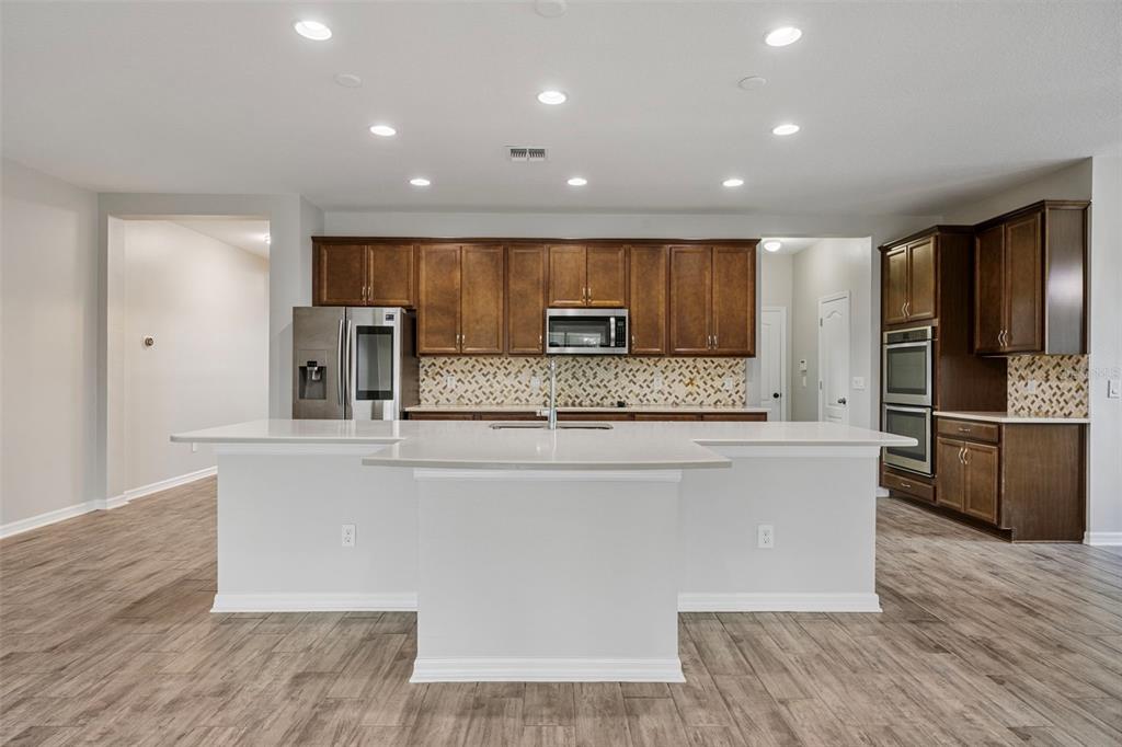 5356 Ragusa Loop St. Cloud, FL 34771 - Photo 26 of 69 a large kitchen with stainless steel appliances kitchen island a large counter top and a stove top oven