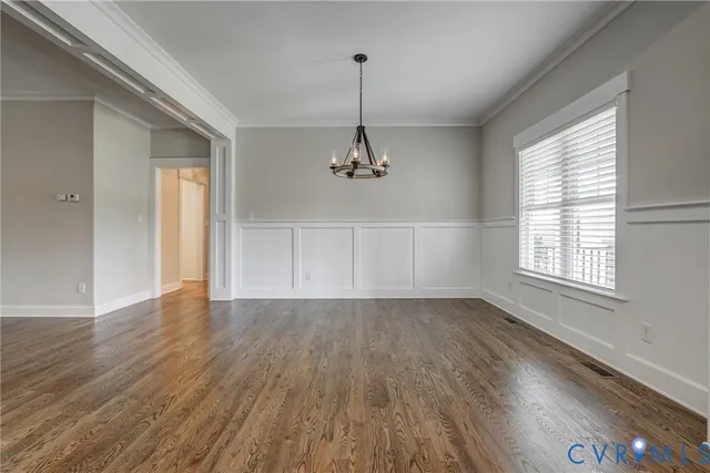 an empty room with wooden floor chandelier and windows