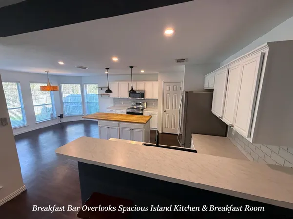 a kitchen with stainless steel appliances a refrigerator a sink dishwasher with a dining table and wooden floor