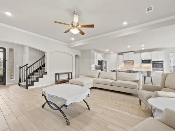 a kitchen with stainless steel appliances granite countertop a stove a sink a refrigerator white cabinets and couches with wooden floor