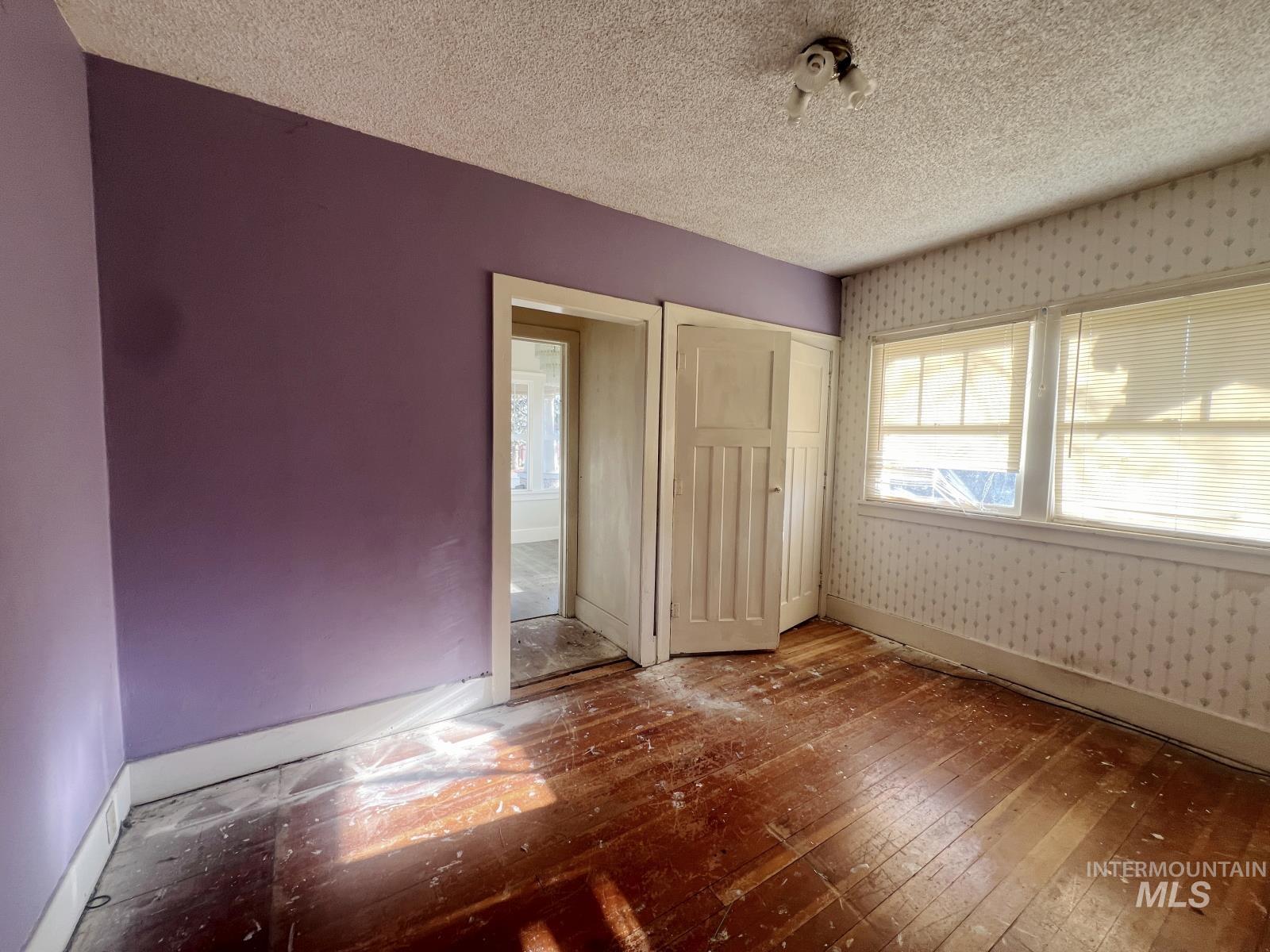 1002 9th Street Clarkston, WA 99403 - Photo 11 of 19 Unfurnished bedroom featuring wood-type flooring, a textured ceiling, a closet, and wallpapered walls