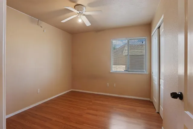 an empty room with wooden floor fan and windows