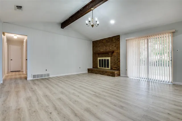 an empty room with wooden floor fireplace and windows