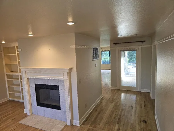 an empty room with wooden floor fireplace and windows