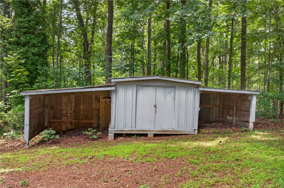 230 Dickard Road Seneca, SC 29672 - Photo 20 of 25 A versatile storage shed with integrated covered wings offers ample space for outdoor equipment, set against a backdrop of mature trees.