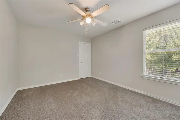 an empty room with a chandelier fan and windows