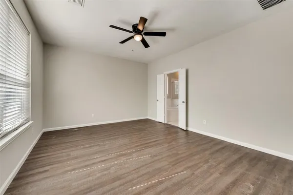an empty room with wooden floor fan and windows