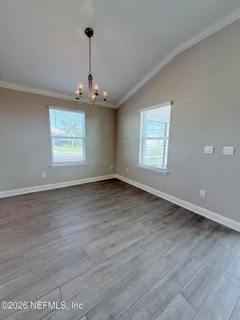 an empty room with wooden floor chandelier and windows