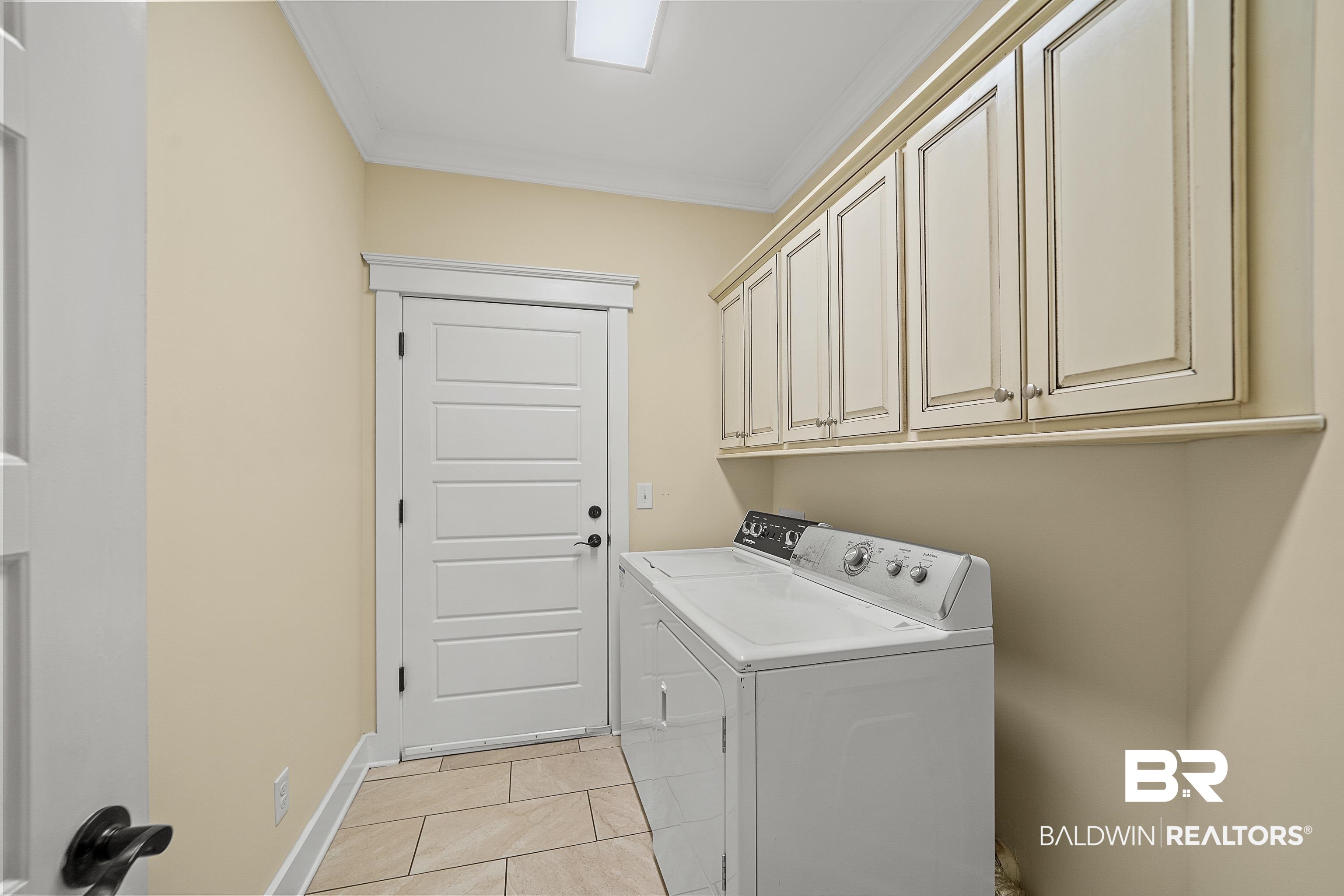 356 Liberty Street Fairhope, AL 36532 - Photo 29 of 39 Laundry room featuring ornamental molding, washing machine and dryer, light tile patterned floors, and cabinet space