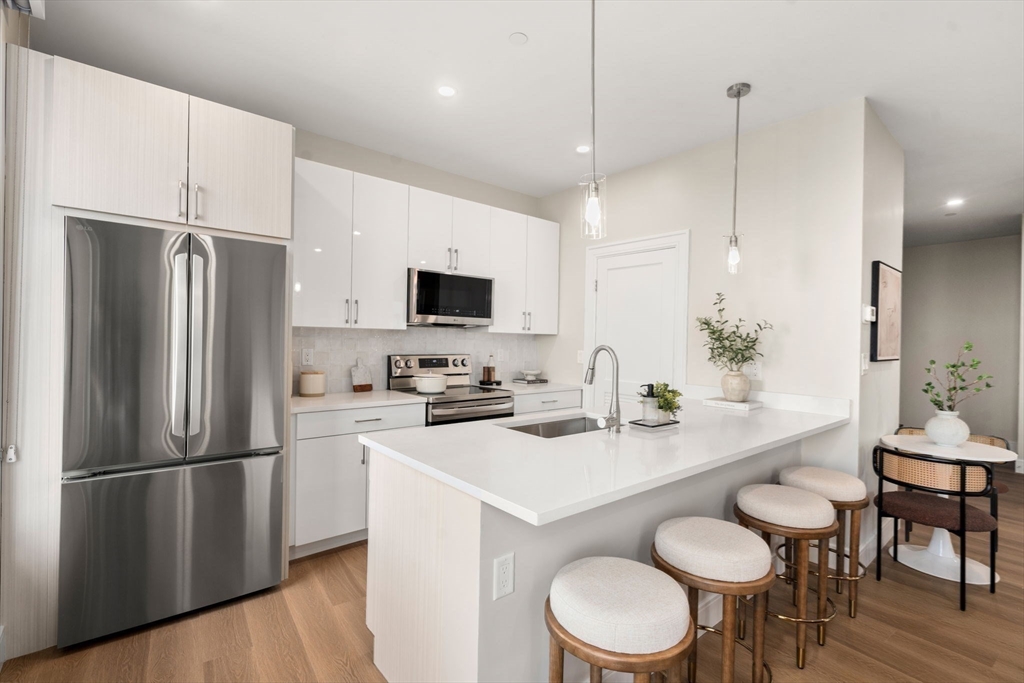40 Soldiers Field Place, Unit 301 Boston, MA 02135 - Photo 5 of 13 a kitchen with stainless steel appliances a refrigerator a stove a sink a dining table and chairs with wooden floor