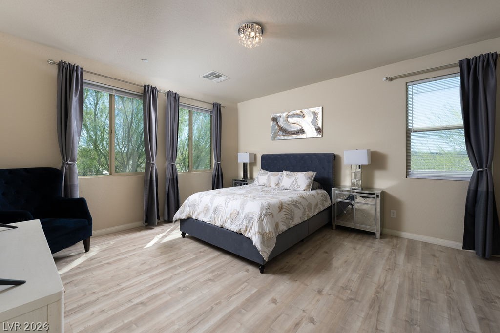 3069 Scenic Rhyme Avenue Henderson, NV 89044 - Photo 12 of 29 The primary suite is genuinely spacious — dual windows, LVP flooring, a crystal flush-mount fixture, and the walk-in closet doorway visible on the far wall. This is the room you picture when you imagine finally having enough space.